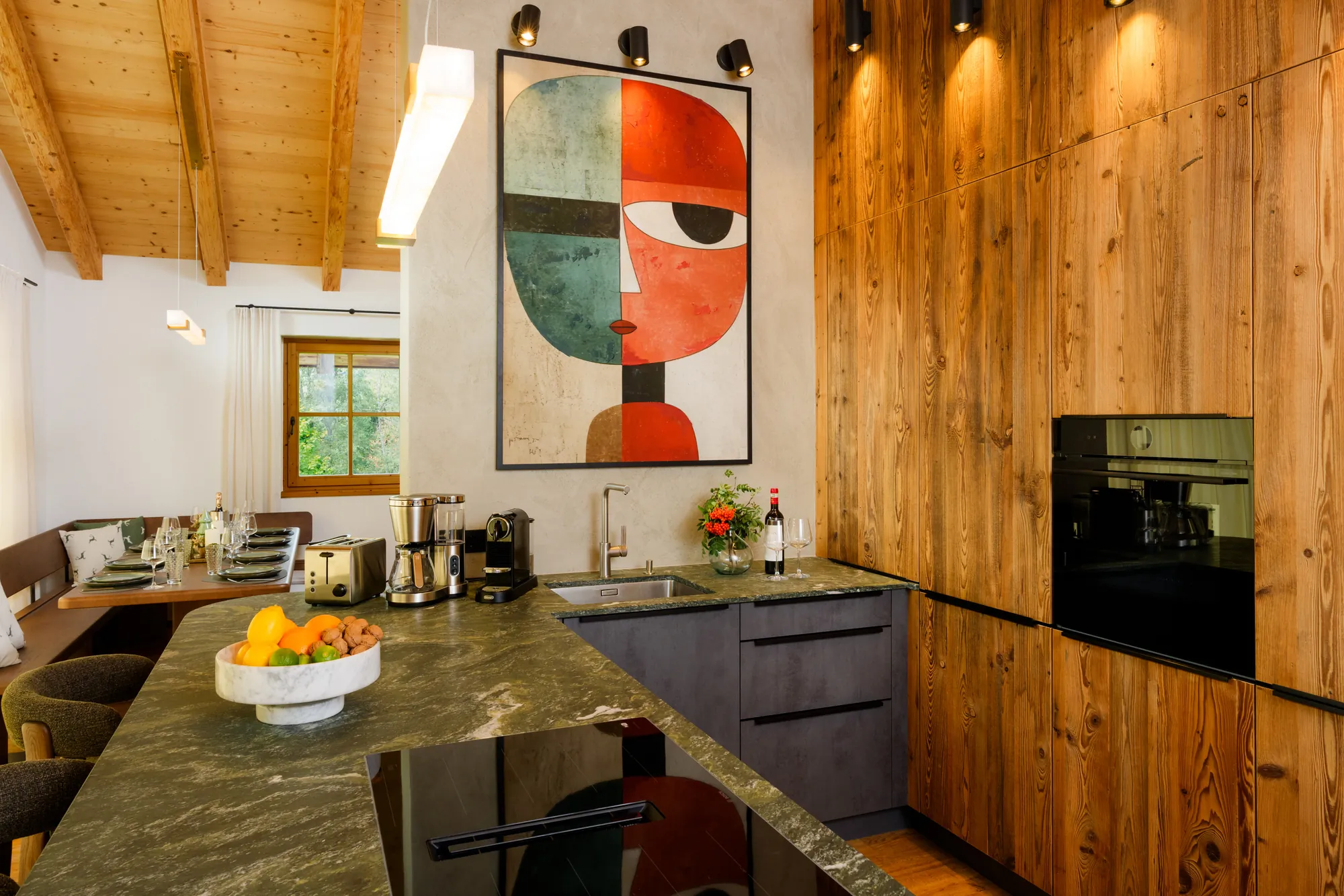 Designküche mit Kochinsel, grüner Steinarbeitsplatte, Holzfronten, Backofen und großem Kunstbild an der Wand