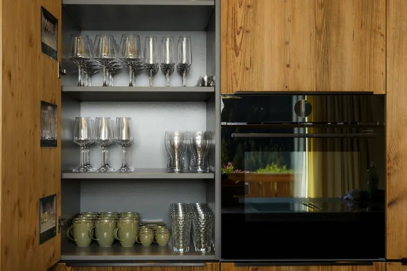 Offener Küchenschrank mit Wein- und Wassergläsern, Tassen und Einbaubackofen in Holzfront