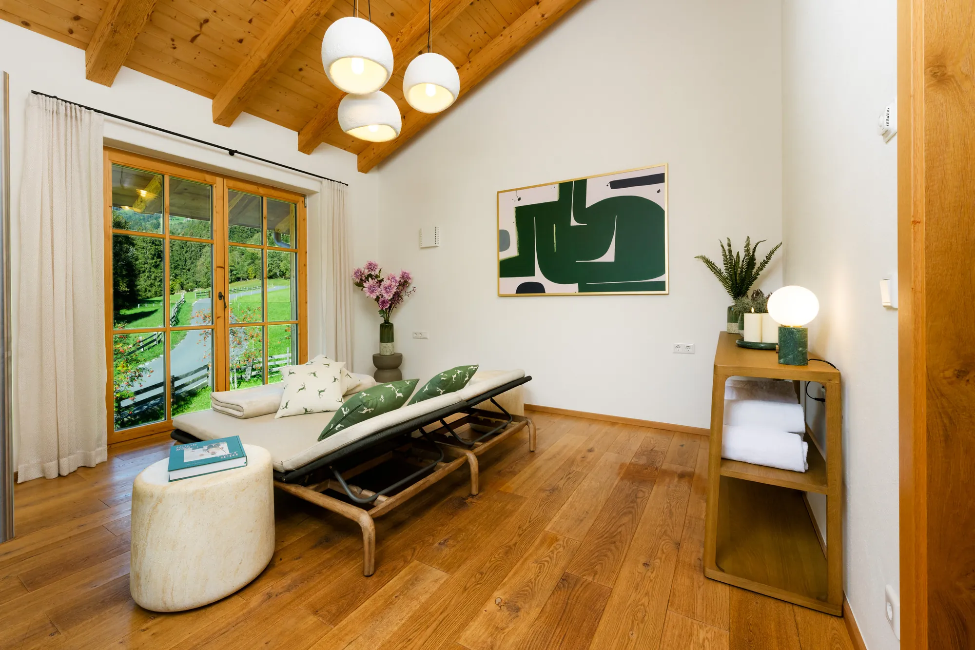 Ruheraum mit zwei Relaxliegen, Kissen mit Hirschmotiv, Handtuchregal, Pflanzen und Fenstertür zum Garten