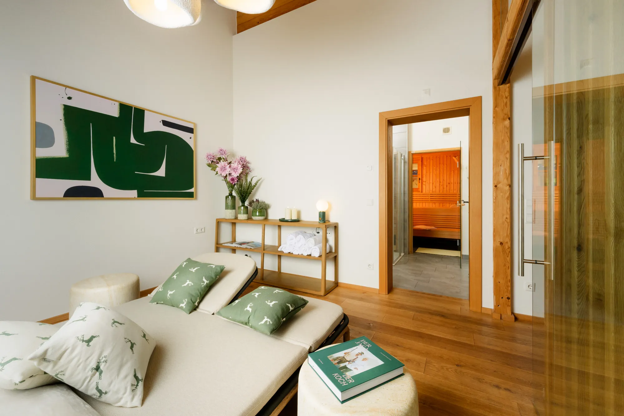 Ruheraum mit Relaxliegen und Hirschkissen, im Hintergrund die offene Tür zur Sauna und ein Handtuchregal
