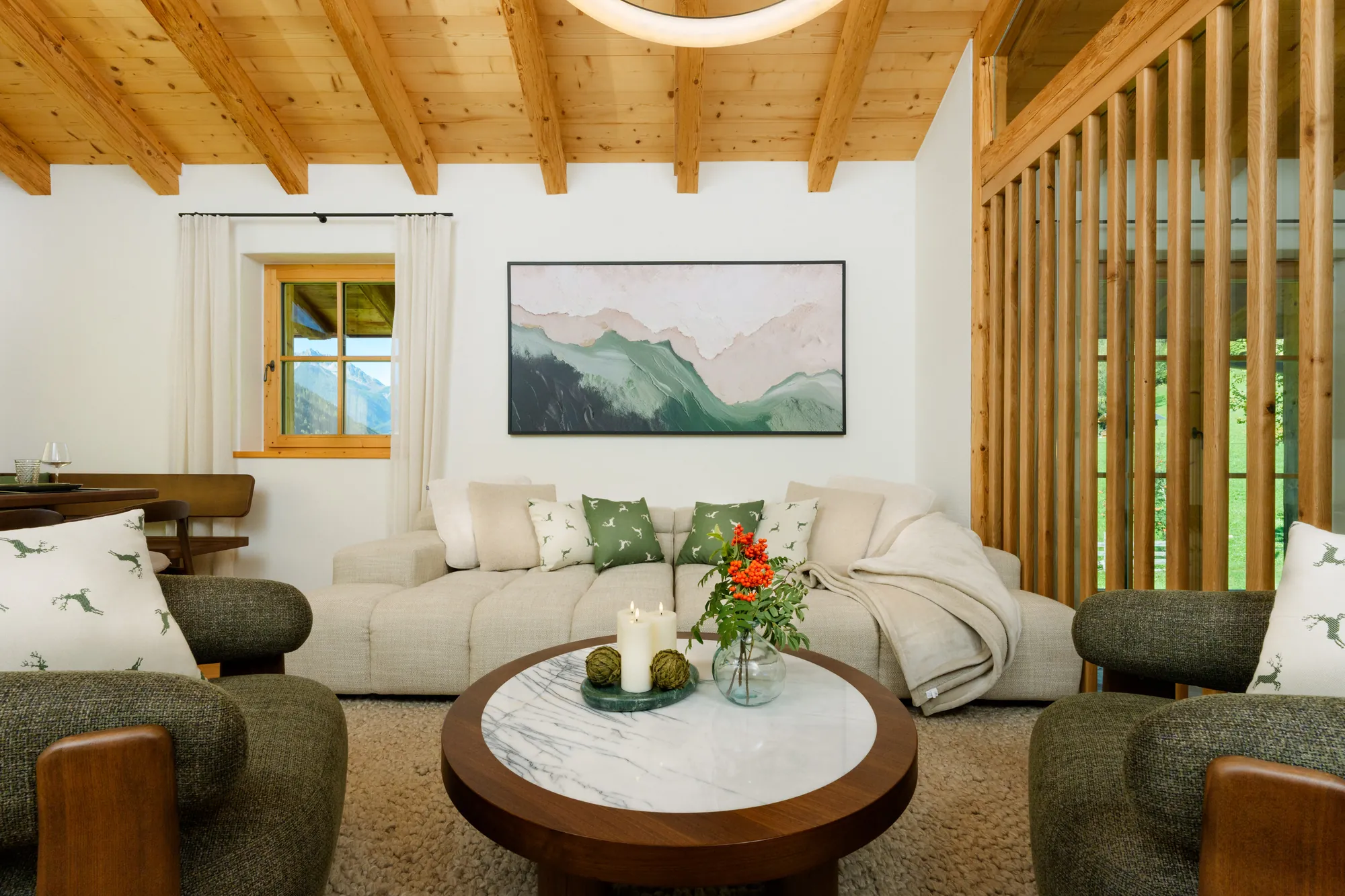 Wohnzimmer mit hellem Sofa, zwei grünen Sesseln, rundem Couchtisch aus Marmor und Holzdecke